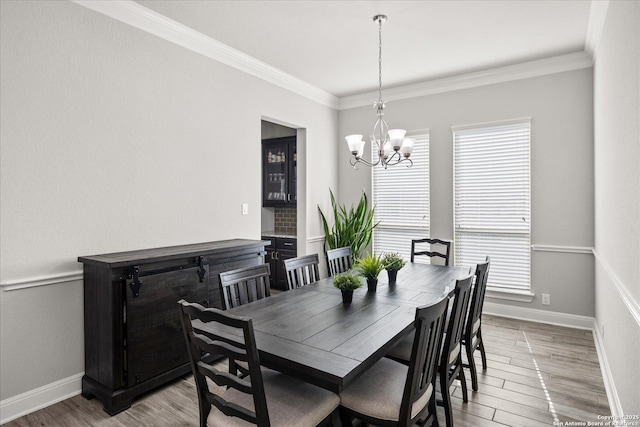 dining space featuring baseboards, ornamental molding, a notable chandelier, and wood finished floors