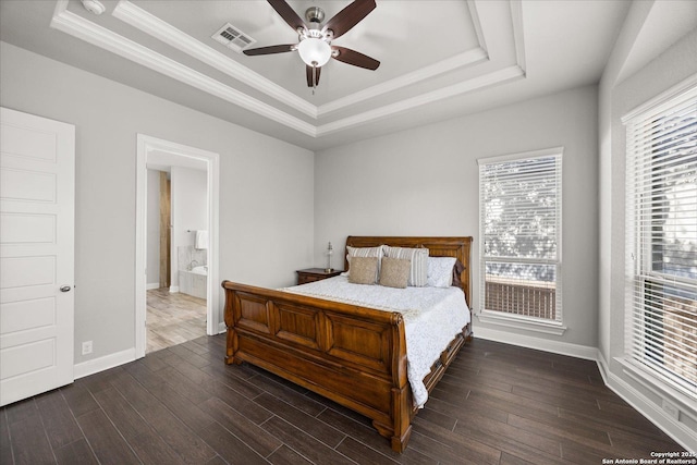 bedroom with a tray ceiling, wood finished floors, visible vents, and baseboards