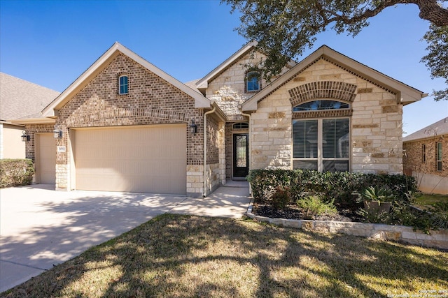 french provincial home with a garage, stone siding, brick siding, and concrete driveway