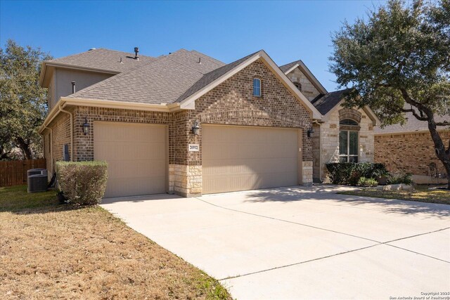 view of front of house with a garage, a shingled roof, central AC unit, stone siding, and brick siding