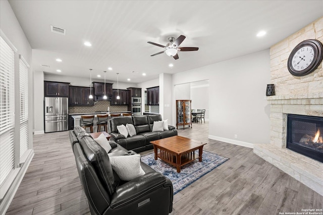 living room with ceiling fan, a fireplace, visible vents, baseboards, and light wood finished floors