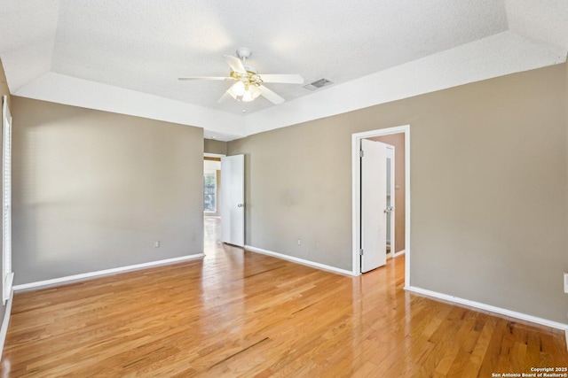 spare room featuring light wood-style floors, visible vents, a textured ceiling, and baseboards