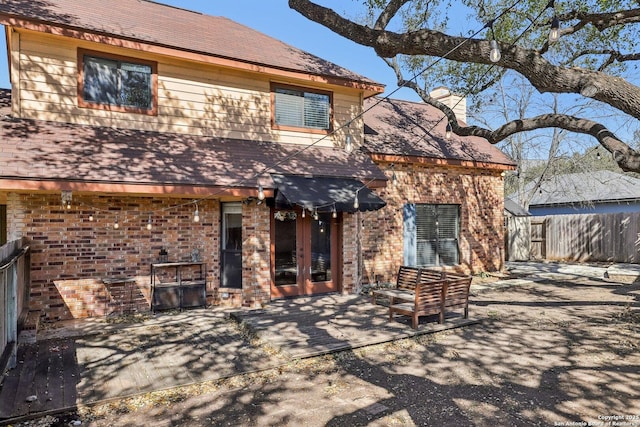 view of front of home featuring a patio, brick siding, a chimney, and fence