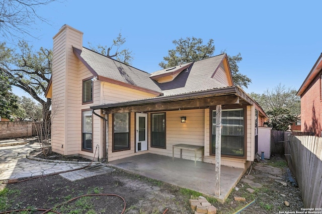 rear view of house with a patio, a shingled roof, a chimney, and a fenced backyard