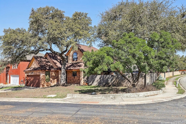 view of front of property featuring driveway, brick siding, an attached garage, and fence