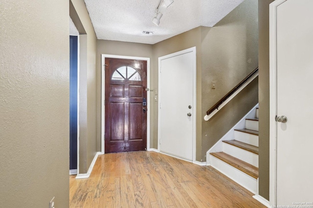 entryway with baseboards, wood finished floors, stairs, a textured ceiling, and track lighting