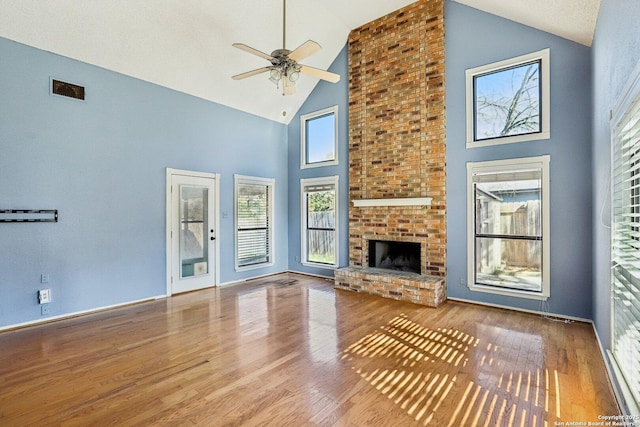 unfurnished living room featuring ceiling fan, a brick fireplace, wood finished floors, and visible vents