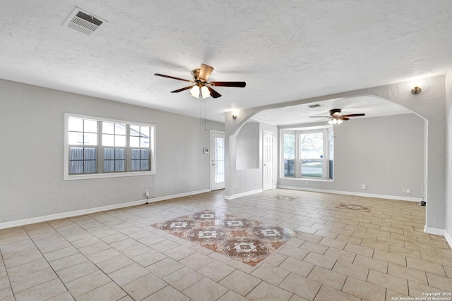 interior space with arched walkways, visible vents, a ceiling fan, a textured ceiling, and tile patterned floors