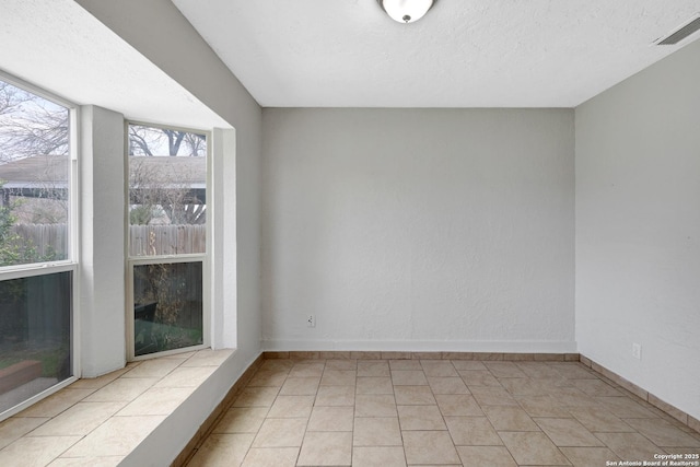 empty room featuring baseboards, visible vents, a textured ceiling, and light tile patterned flooring