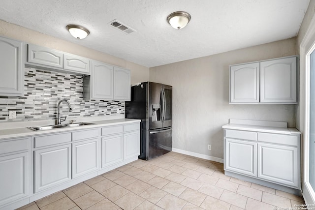 kitchen with light countertops, visible vents, decorative backsplash, a sink, and refrigerator with ice dispenser