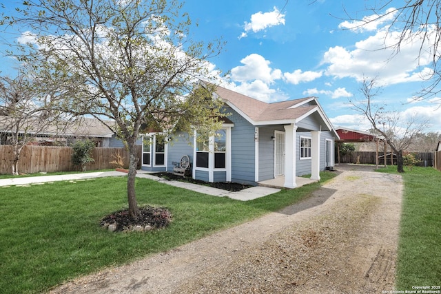 view of front of property with a shingled roof, dirt driveway, fence, and a front lawn