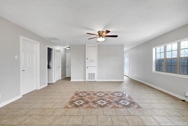 empty room featuring a textured ceiling, light tile patterned flooring, a ceiling fan, and baseboards