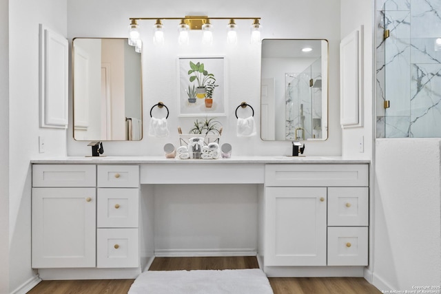 full bathroom featuring double vanity, a marble finish shower, baseboards, wood finished floors, and a sink