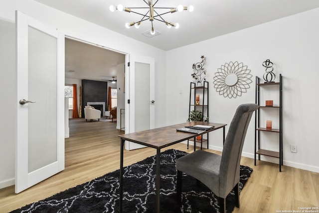 home office with light wood-style floors, a fireplace, baseboards, and an inviting chandelier