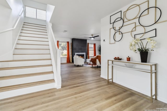 entrance foyer featuring a large fireplace, visible vents, light wood-style flooring, ceiling fan, and stairway