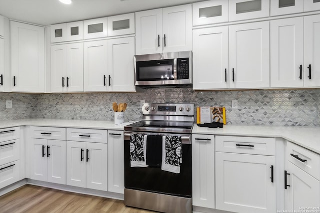 kitchen with stainless steel appliances, light countertops, backsplash, light wood-style flooring, and white cabinetry