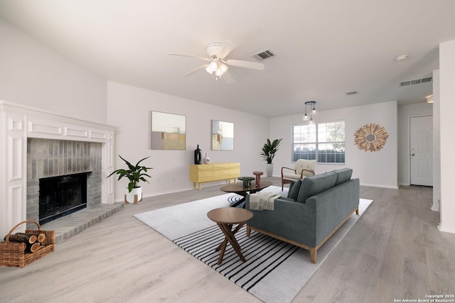 living room featuring baseboards, visible vents, a fireplace with raised hearth, and wood finished floors