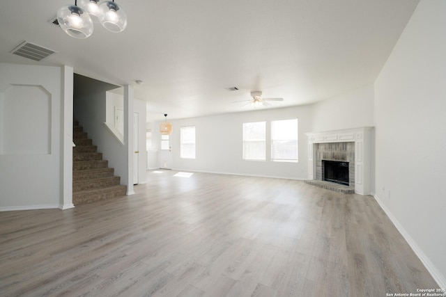 unfurnished living room with stairway, a brick fireplace, visible vents, and light wood-style floors