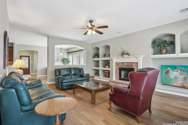 living area featuring built in shelves, a ceiling fan, a fireplace, and wood finished floors