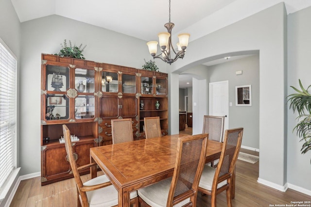 dining space featuring arched walkways, a notable chandelier, lofted ceiling, light wood-style floors, and baseboards