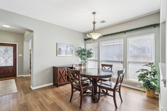 dining room with a wealth of natural light, arched walkways, visible vents, and wood finished floors