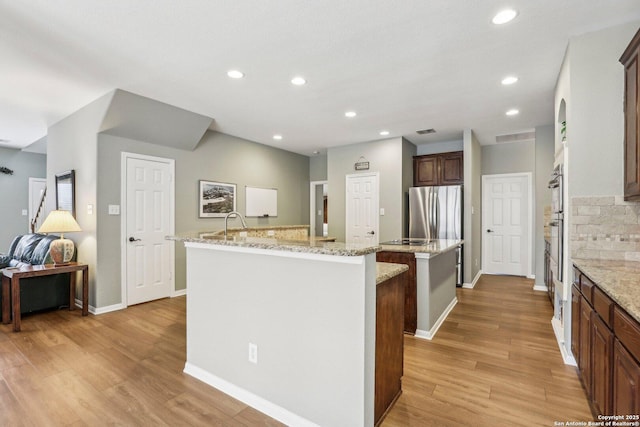 kitchen with tasteful backsplash, freestanding refrigerator, a kitchen island with sink, light wood-style floors, and recessed lighting