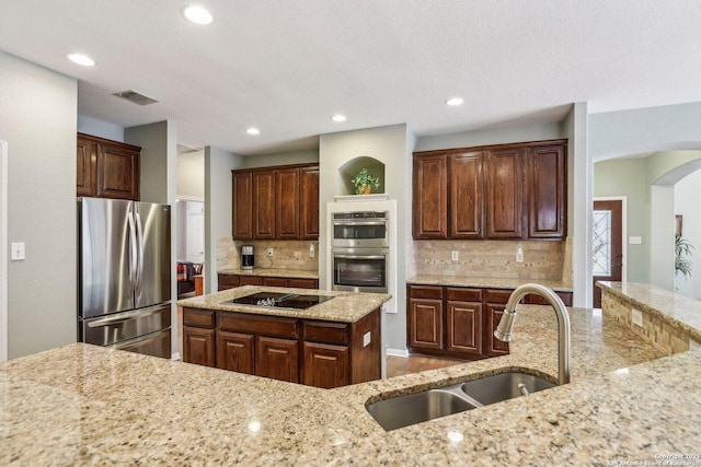 kitchen with arched walkways, visible vents, light stone counters, stainless steel appliances, and a sink