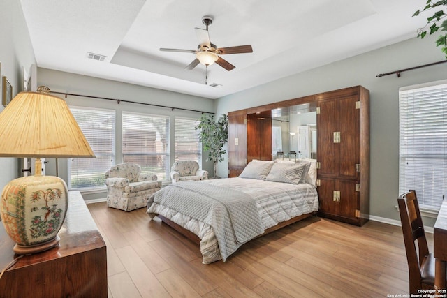 bedroom with baseboards, visible vents, a ceiling fan, wood finished floors, and a tray ceiling