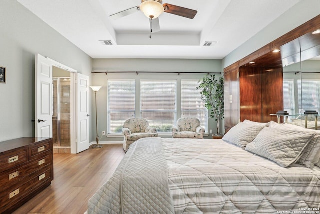 bedroom with a raised ceiling, visible vents, multiple windows, and wood finished floors