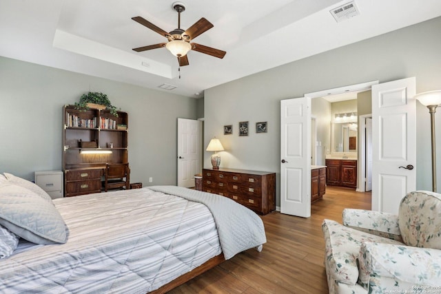 bedroom with ceiling fan, ensuite bathroom, wood finished floors, visible vents, and a tray ceiling