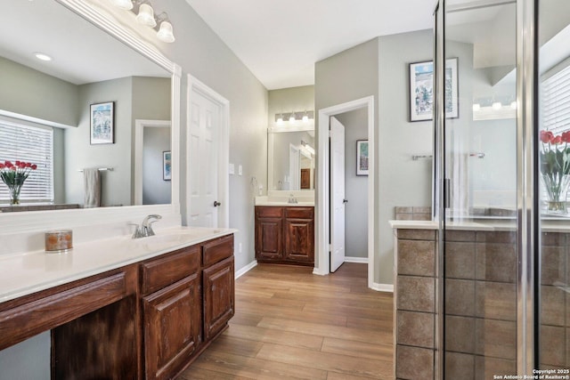 full bathroom featuring wood finished floors, two vanities, a sink, and baseboards