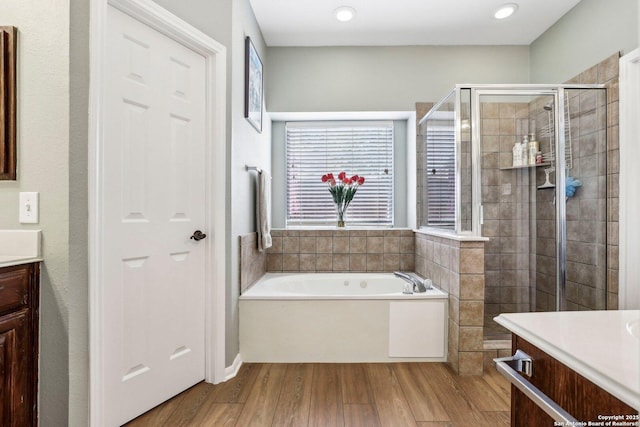 full bathroom featuring a stall shower, a garden tub, vanity, and wood finished floors