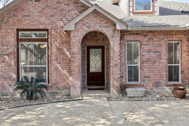 property entrance featuring brick siding and roof with shingles