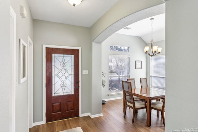 foyer entrance featuring visible vents, arched walkways, dark wood finished floors, baseboards, and a chandelier