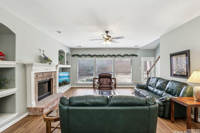 living room with a brick fireplace, ceiling fan, baseboards, and wood finished floors