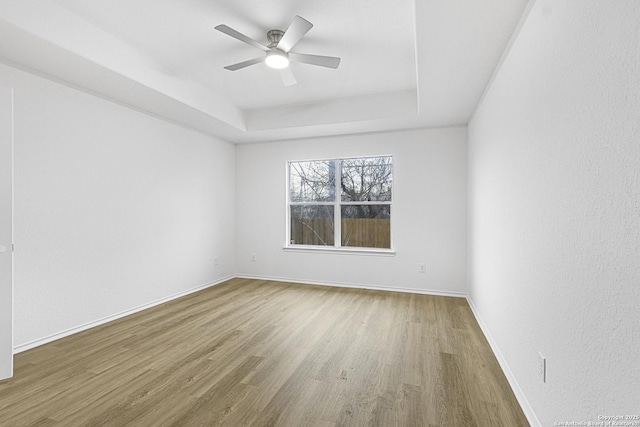 unfurnished room featuring ceiling fan, a tray ceiling, wood finished floors, and baseboards