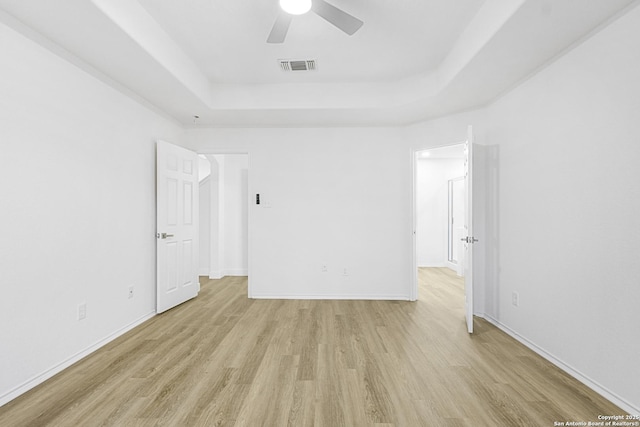 spare room with ceiling fan, visible vents, baseboards, light wood-style floors, and a raised ceiling