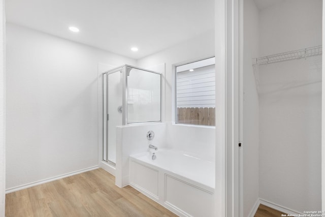 bathroom with a stall shower, wood finished floors, a bath, and a walk in closet