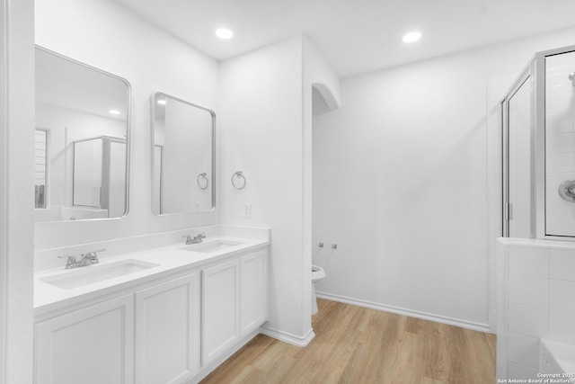 bathroom with double vanity, toilet, an enclosed shower, a sink, and wood finished floors