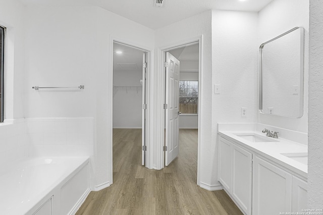 bathroom featuring a garden tub, a sink, wood finished floors, double vanity, and a walk in closet