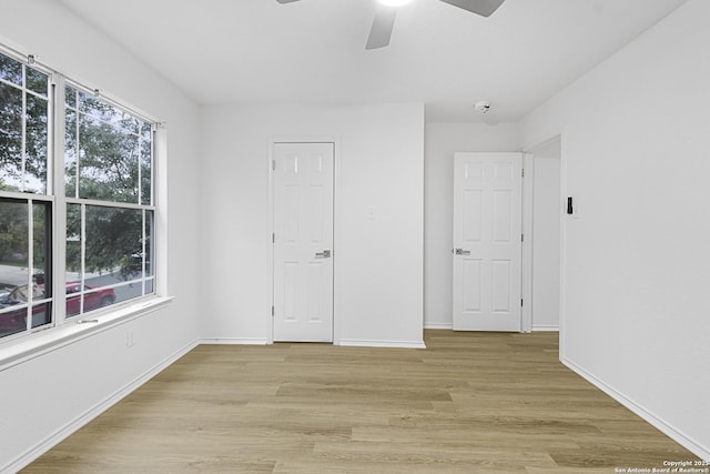 unfurnished bedroom with ceiling fan, multiple windows, light wood-style flooring, and baseboards