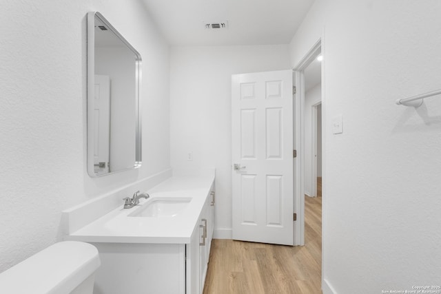 half bathroom with toilet, vanity, wood finished floors, and visible vents