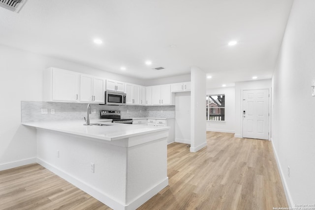 kitchen with stainless steel appliances, tasteful backsplash, light countertops, a sink, and a peninsula