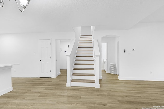 stairs featuring baseboards, visible vents, arched walkways, wood finished floors, and a textured ceiling