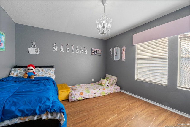 bedroom with baseboards, an inviting chandelier, and wood finished floors