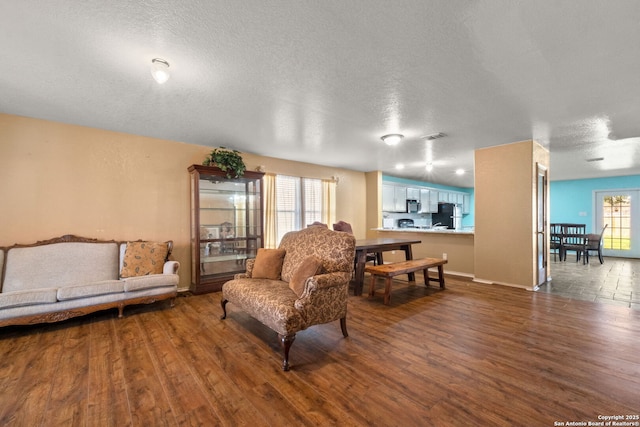 living room featuring baseboards, a textured ceiling, visible vents, and wood finished floors