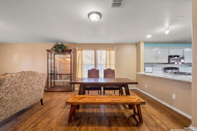 dining room featuring baseboards, a textured ceiling, visible vents, and wood finished floors