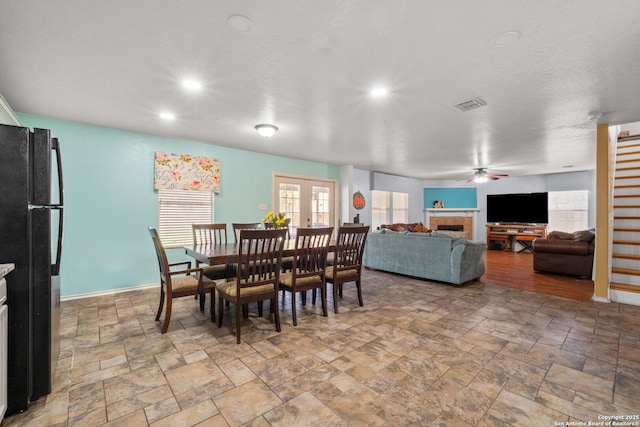 dining room featuring french doors, visible vents, stone finish floor, a tile fireplace, and baseboards