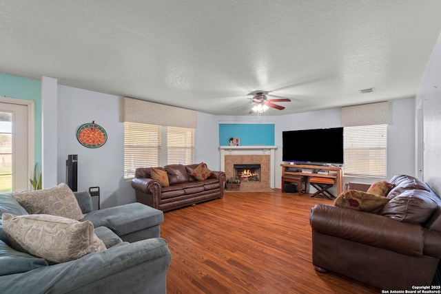 living area featuring visible vents, a ceiling fan, a tile fireplace, wood finished floors, and a textured ceiling