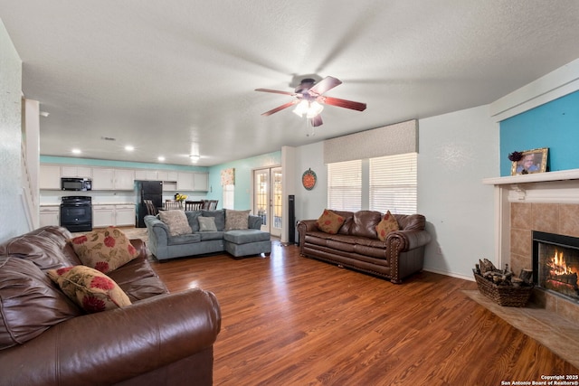 living room with a tile fireplace, ceiling fan, a textured ceiling, and wood finished floors